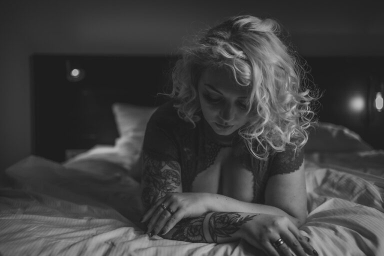 Frau mit Locken und Tattoos liegt auf einem hellen Bett, Schwarzweiß