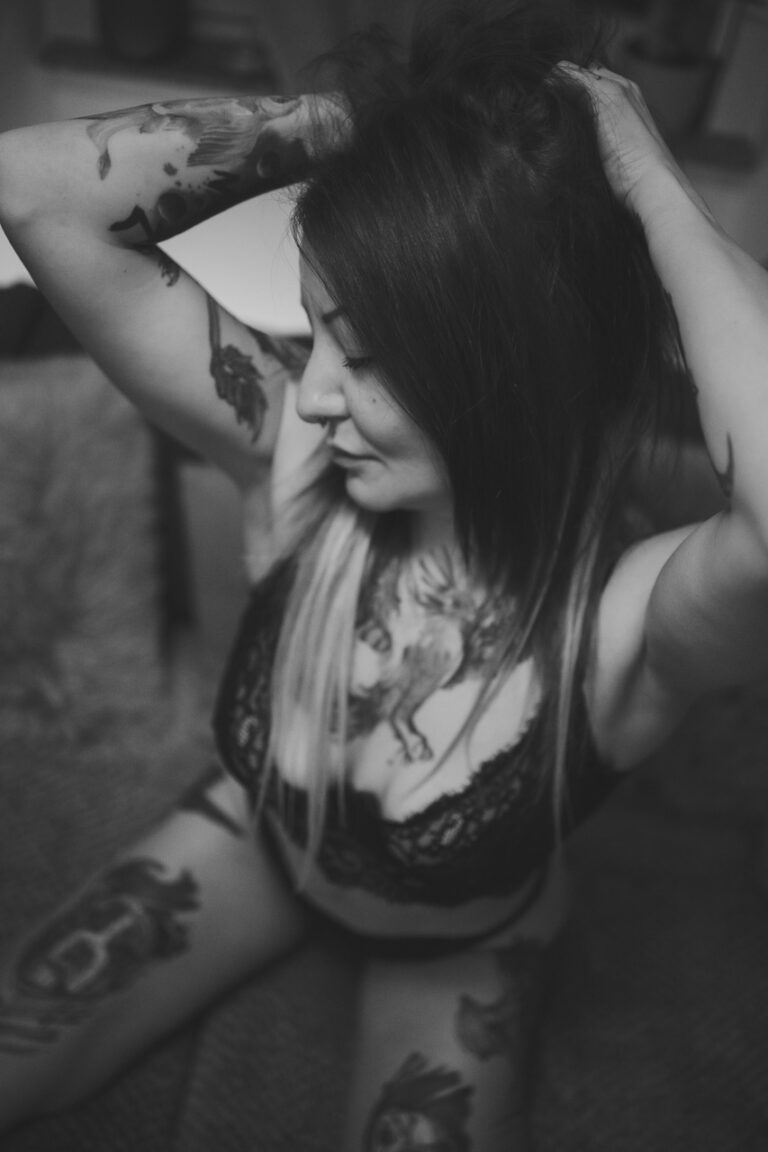 Frau mit Tattoos sitzt auf einem Fellteppich, Schwarzweiß